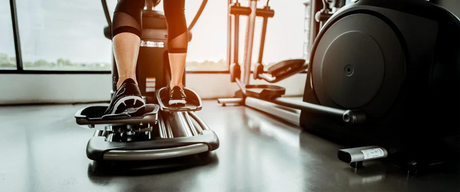 An image showing the lower section of two elliptical machines in a gym, with a woman using the one on the left.