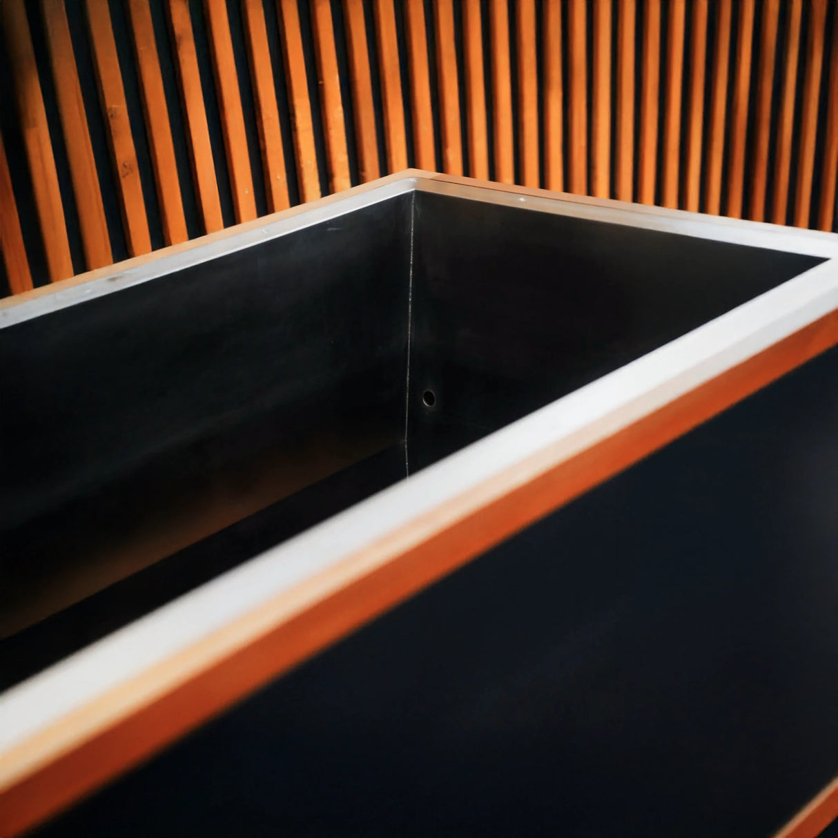 Black cold plunge with stainless steel interior and a wooden trim on the outside