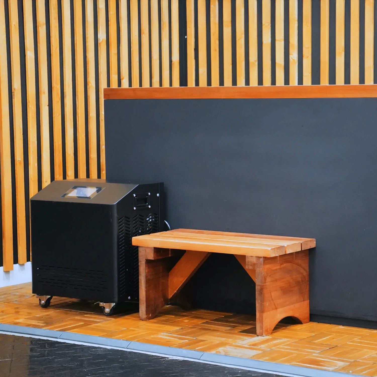 Black cold plunge with a wooden step stool and a black chiller next to it