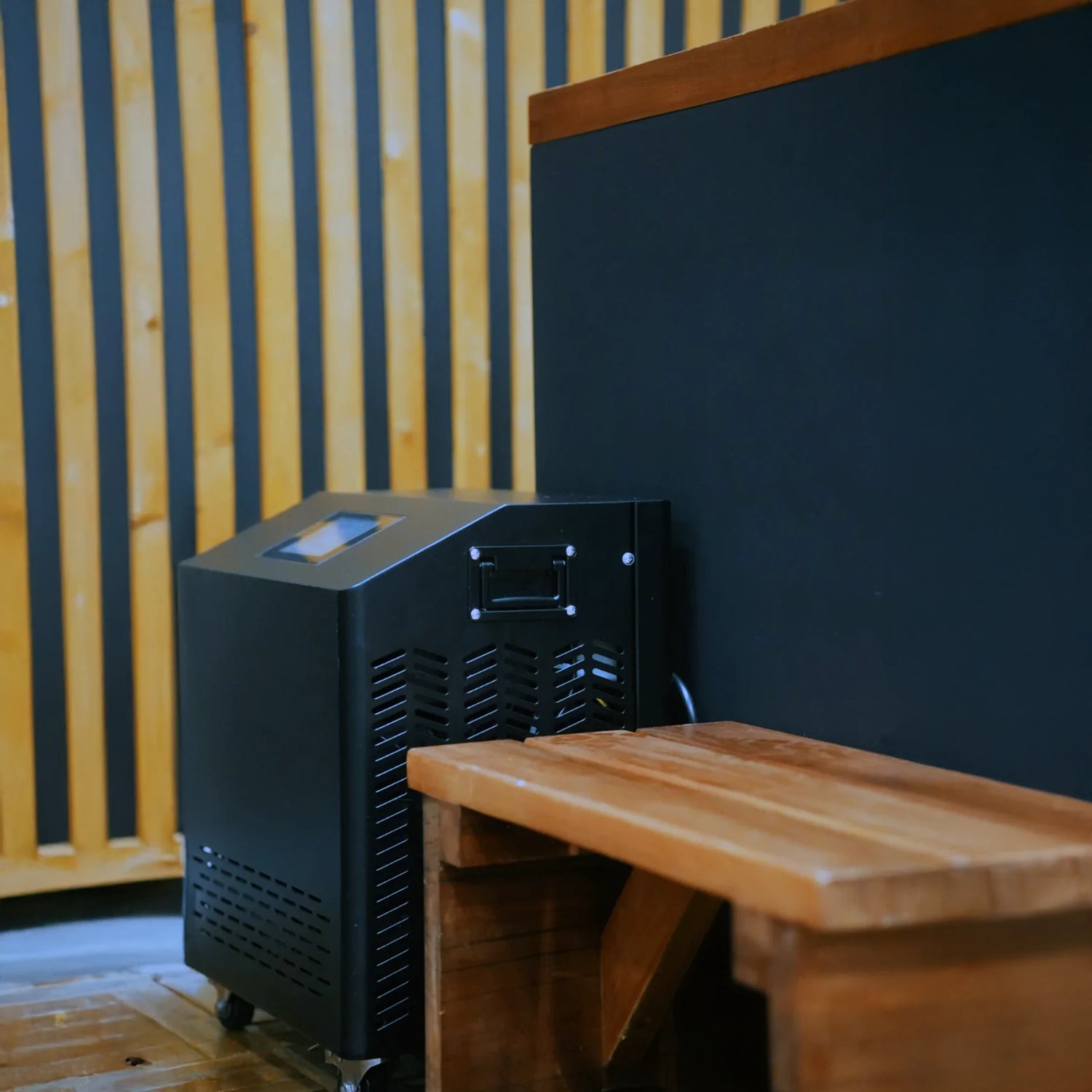 Black cold plunge with a wooden step stool and a black chiller next to it
