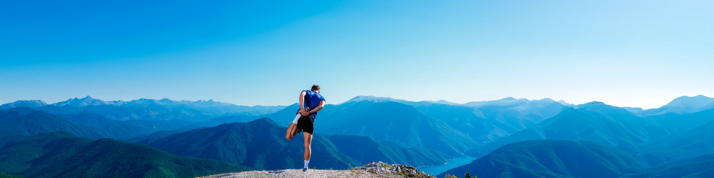 Man standing on a mountain peak with a clear blue sky and distant mountains.