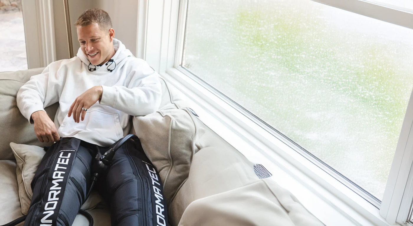 Christian McCaffrey lying on a couch wearing Normatec 3 Legs