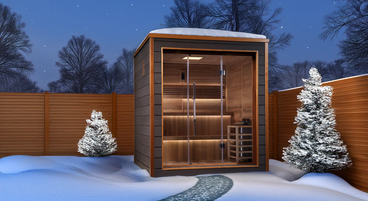 Bergen model sauna with a 6 person capacity made from Canadian red cedar on the interior and dark all weather composite on the exterior built to withstand harsh outdoor weather in a back yard covered in snow.