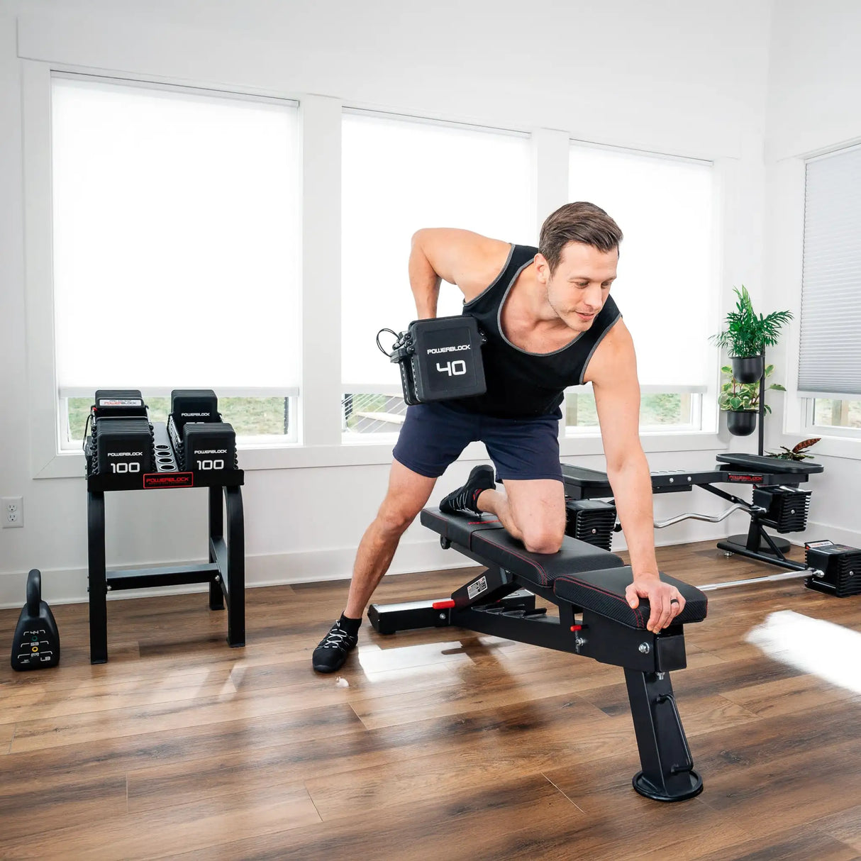 A man doing dumbbell rows while kneeling with one leg on a black PowerBlock utility bench