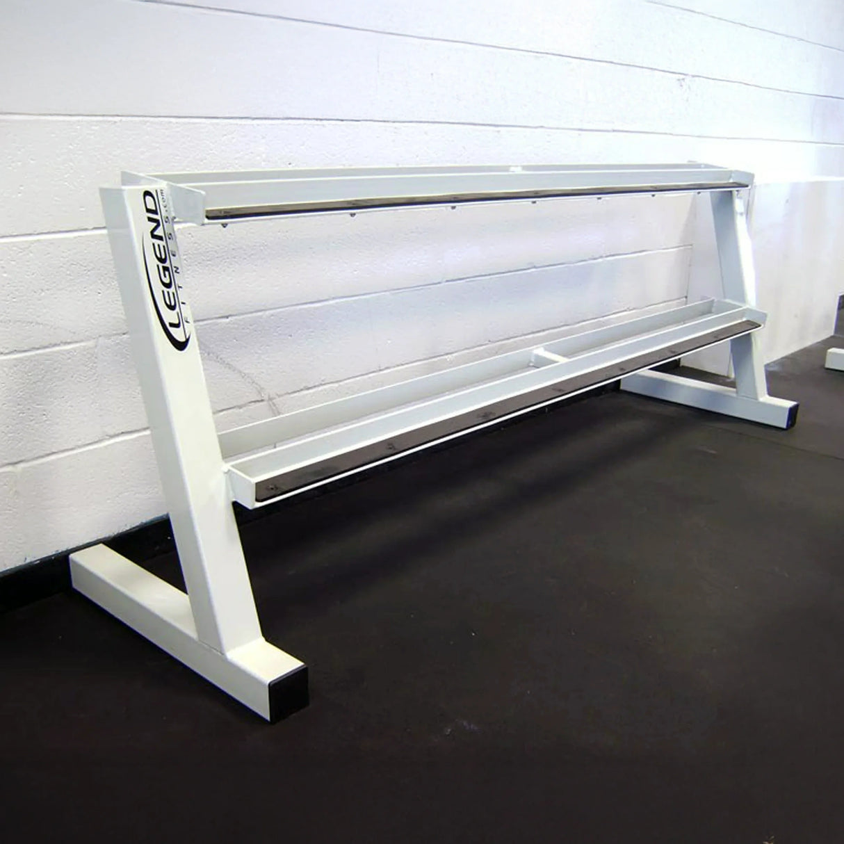 A white empty dumbbell rack against a white wall on a black rubber floor
