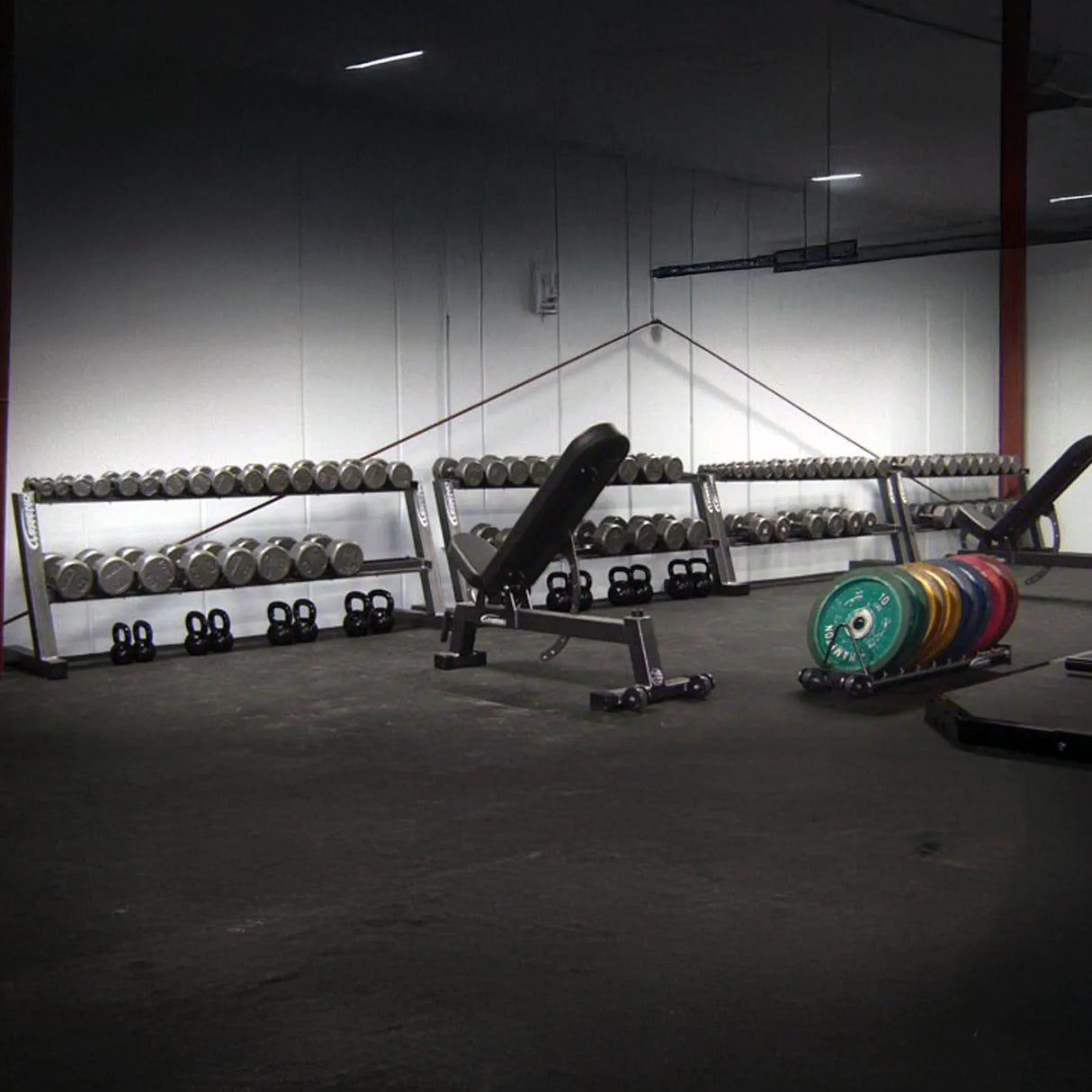 Gym interior with weight racks and dumbbells on a concrete floor.