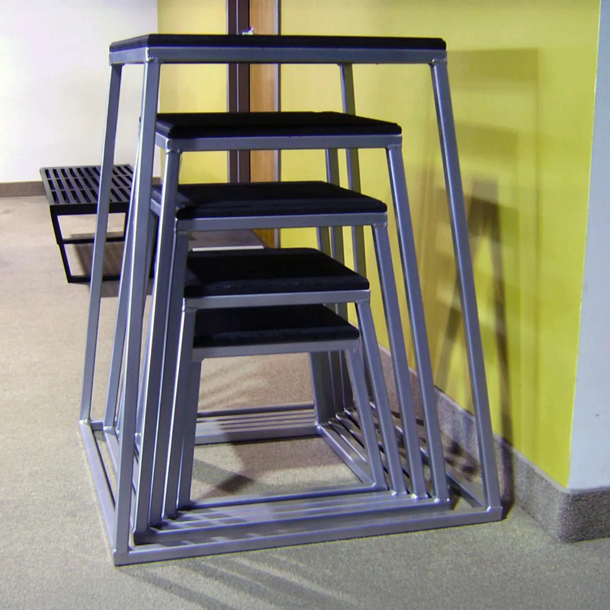Set of metal step stools with black seats against a yellow wall.