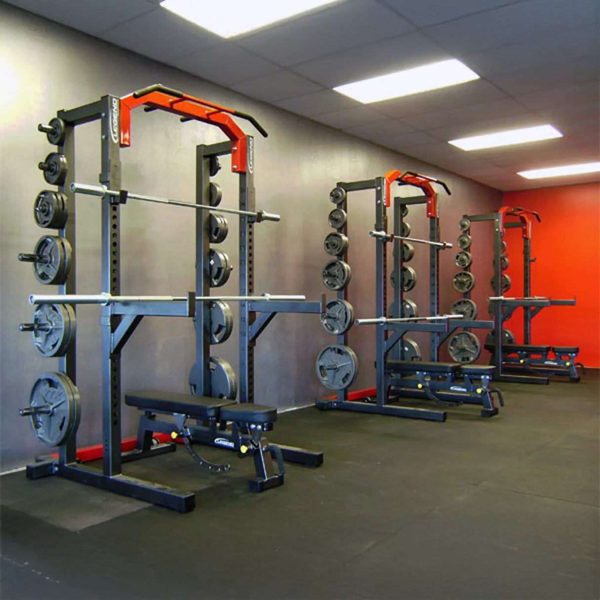 Gym equipment including weight racks and benches in a room with orange walls.