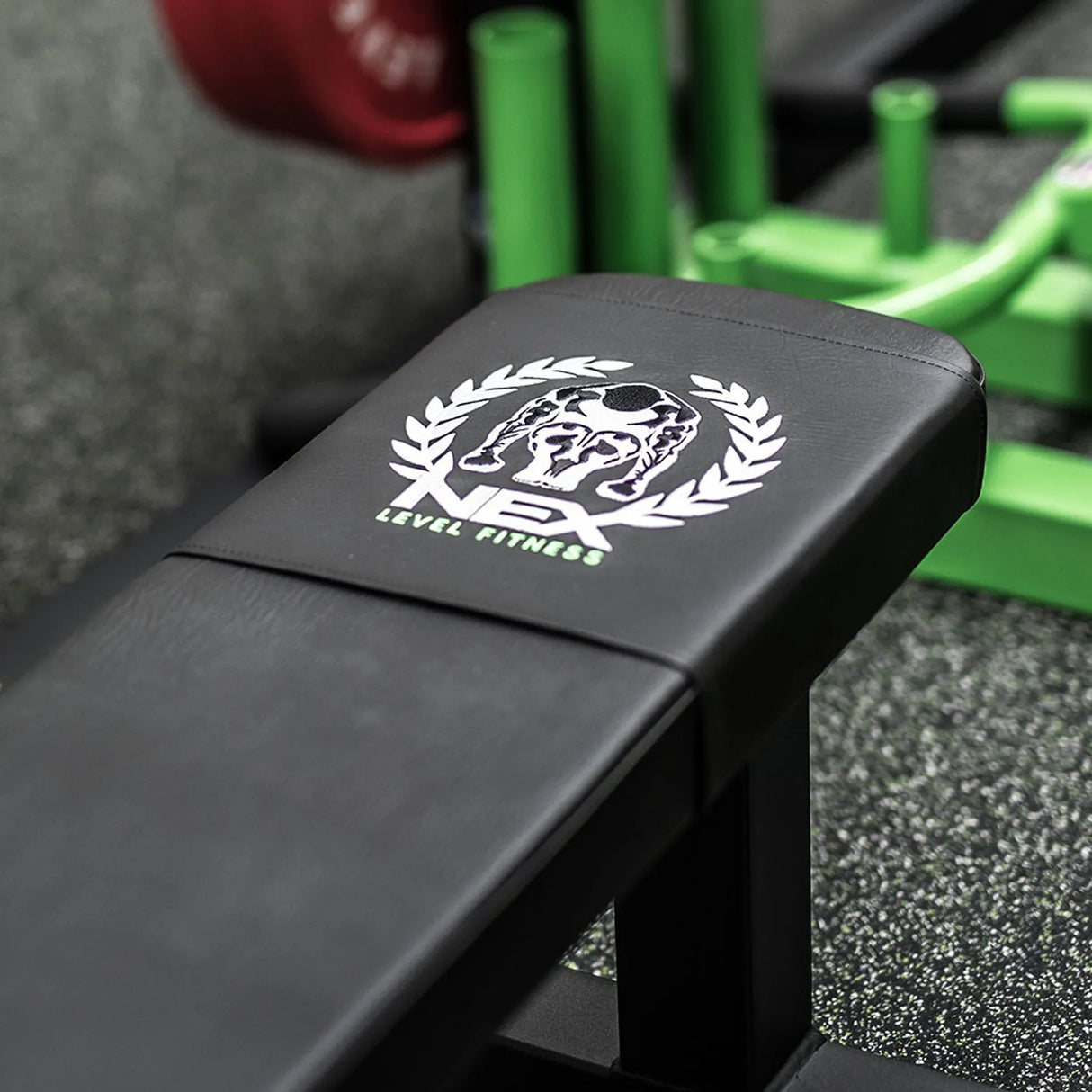 Black gym bench with a logo on it for 'Nex Level Fitness', set against a gym background.