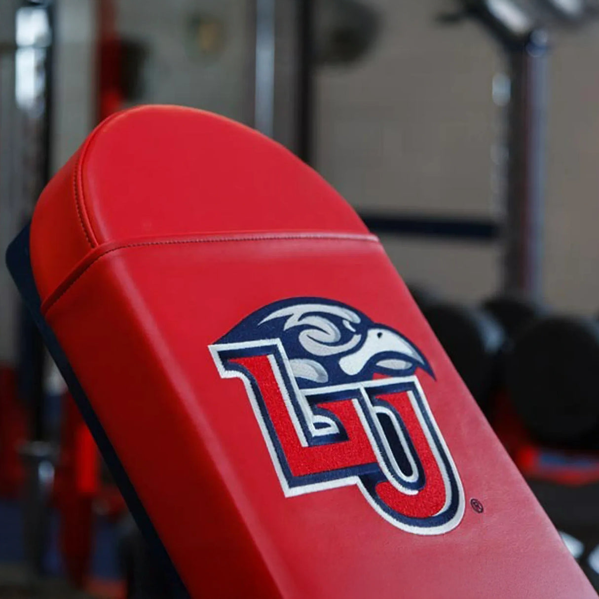 Red weight bench with a blue, red, and white 'LU' logo on it in a gym setting