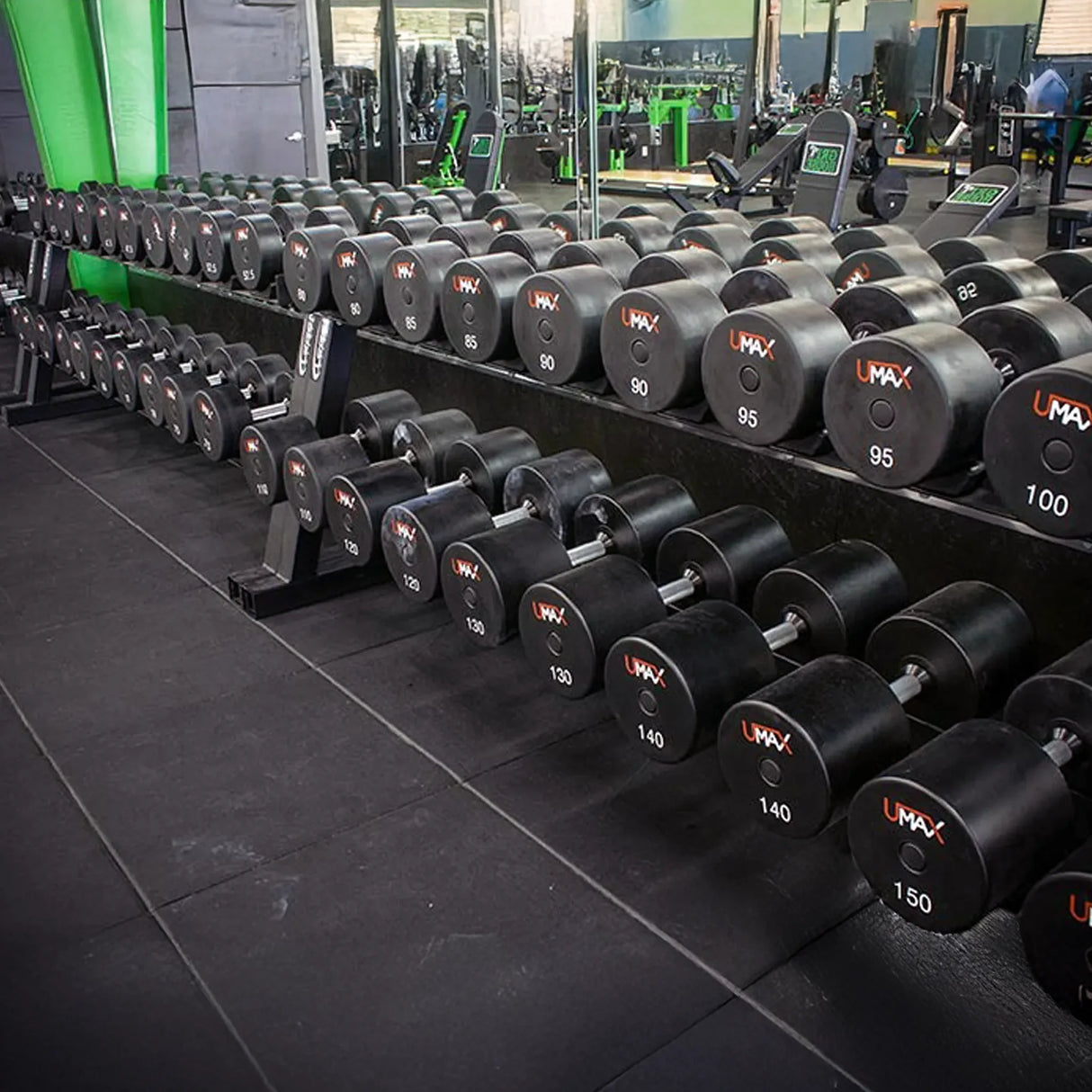 Row of UMAX dumbbells on two black dumbbell storage racks in a gym setting