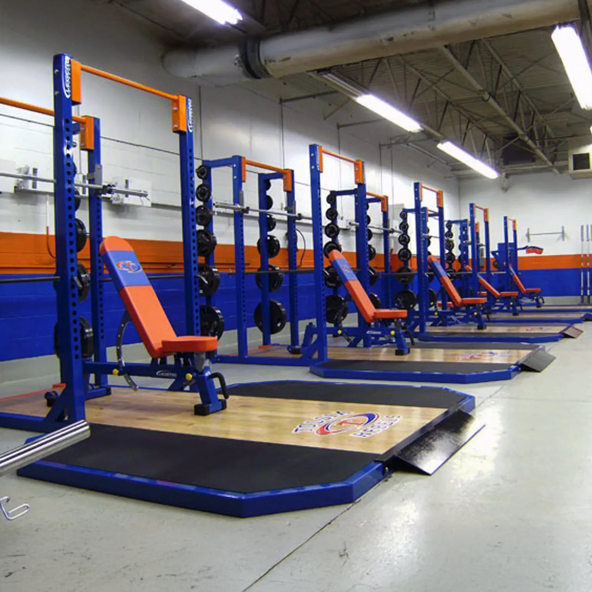 Gym with blue weight racks and orange benches in a well-lit indoor facility.