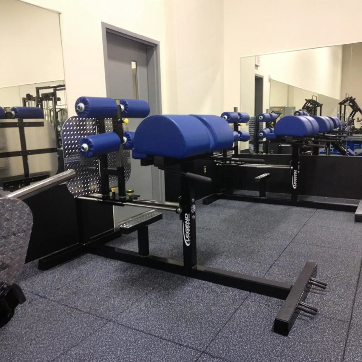 A black glute ham developer fitness machine with blue pads in a gym setting