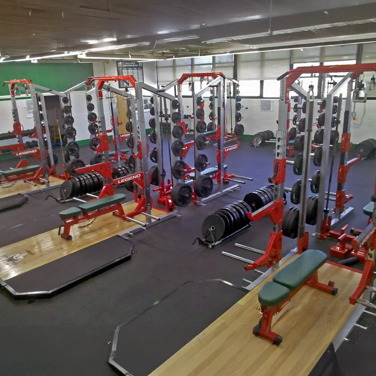 Gym interior with weight lifting equipment including benches, squat racks, platforms, and barbells.