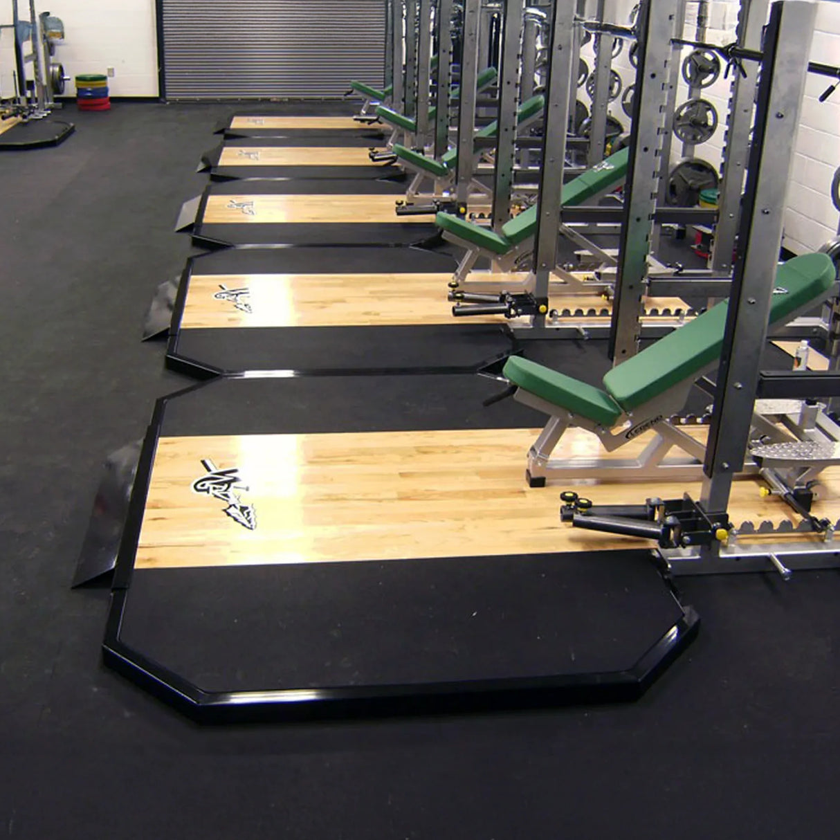 Gym equipment with weight plates, wooden platforms, and benches on a black floor.