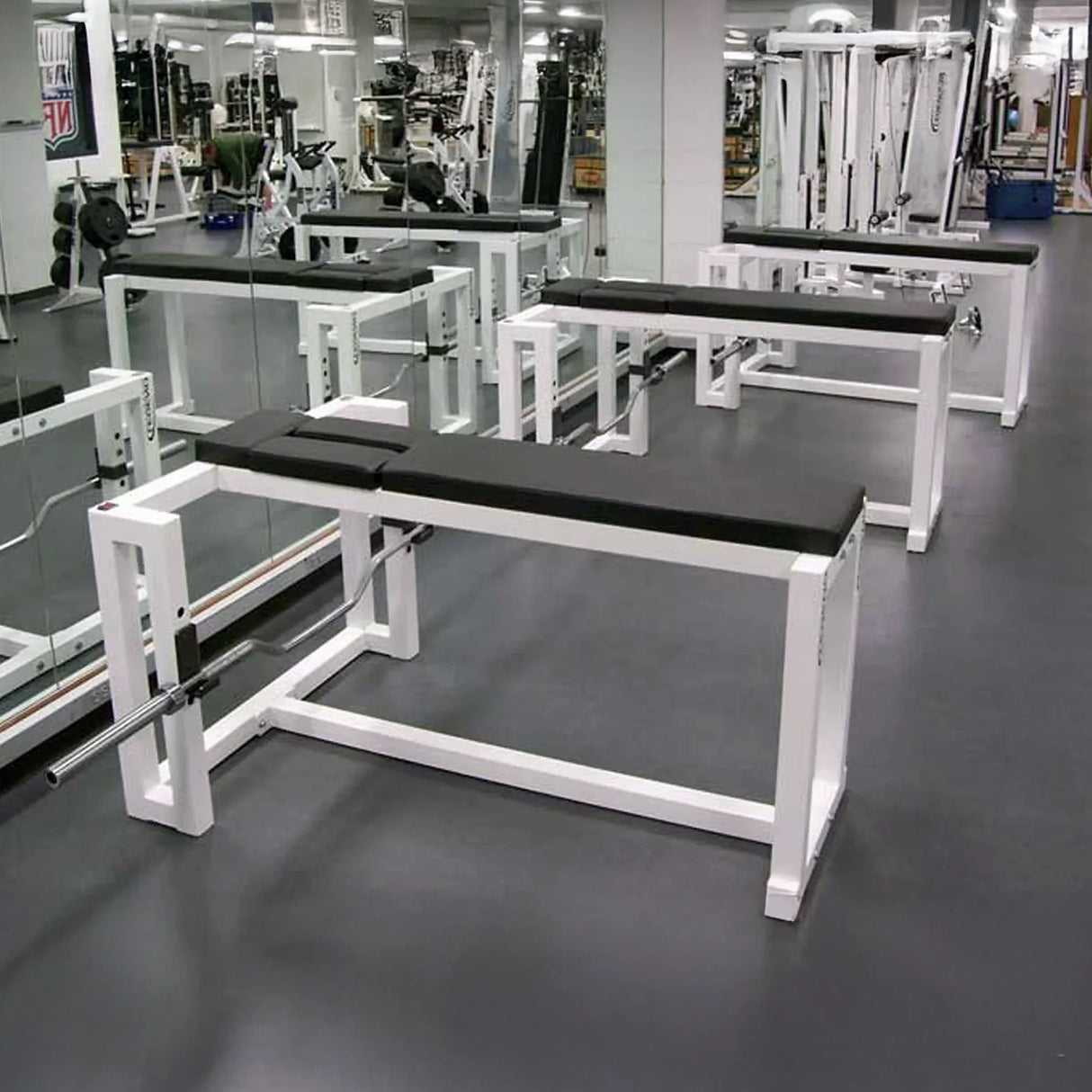 A row of three black and white prone row weightlifting benches in a gym setting