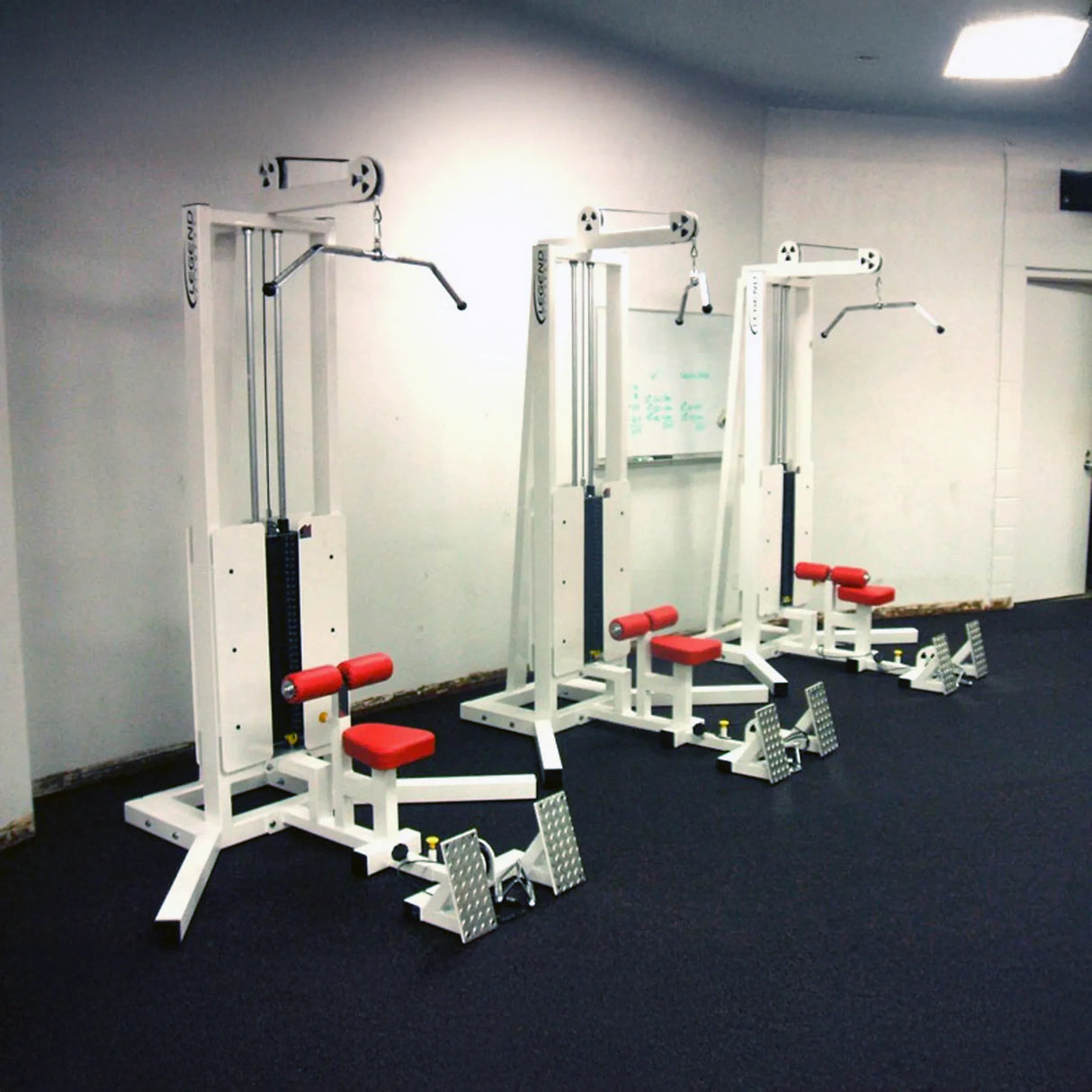 A row of three white lat pulldown floor row gym machines in a gym