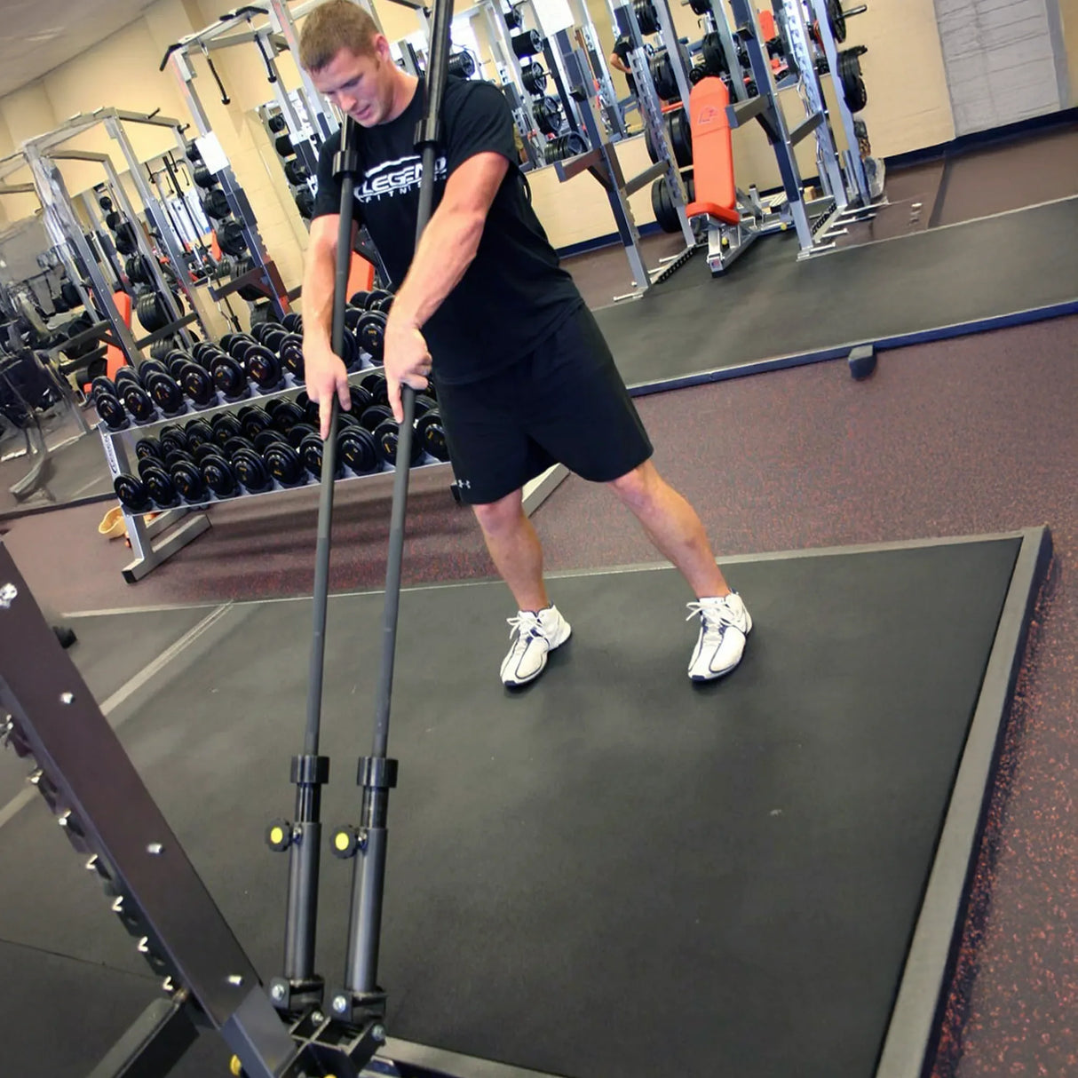 A man exercising while holding one barbell in each hand which are stowed in a metal dual landmine attachment mounted to a squat