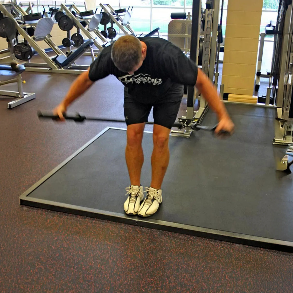A man exercising while holding one barbell in each hand which are stowed in a metal dual landmine attachment mounted to a squat