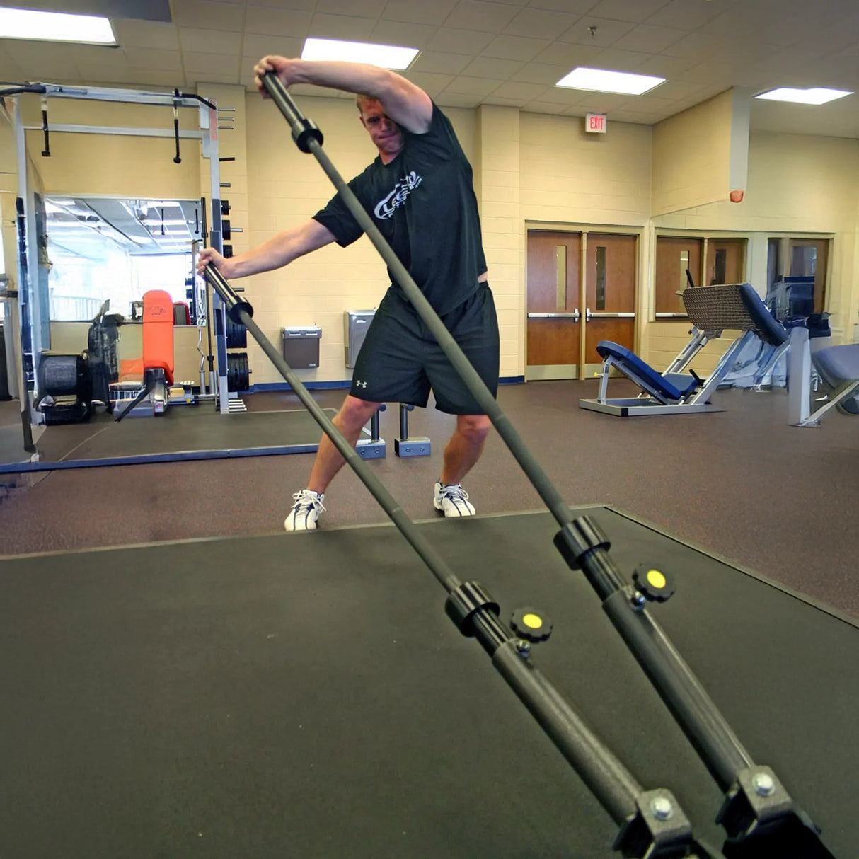 A man exercising while holding one barbell in each hand which are stowed in a metal dual landmine attachment mounted to a squat