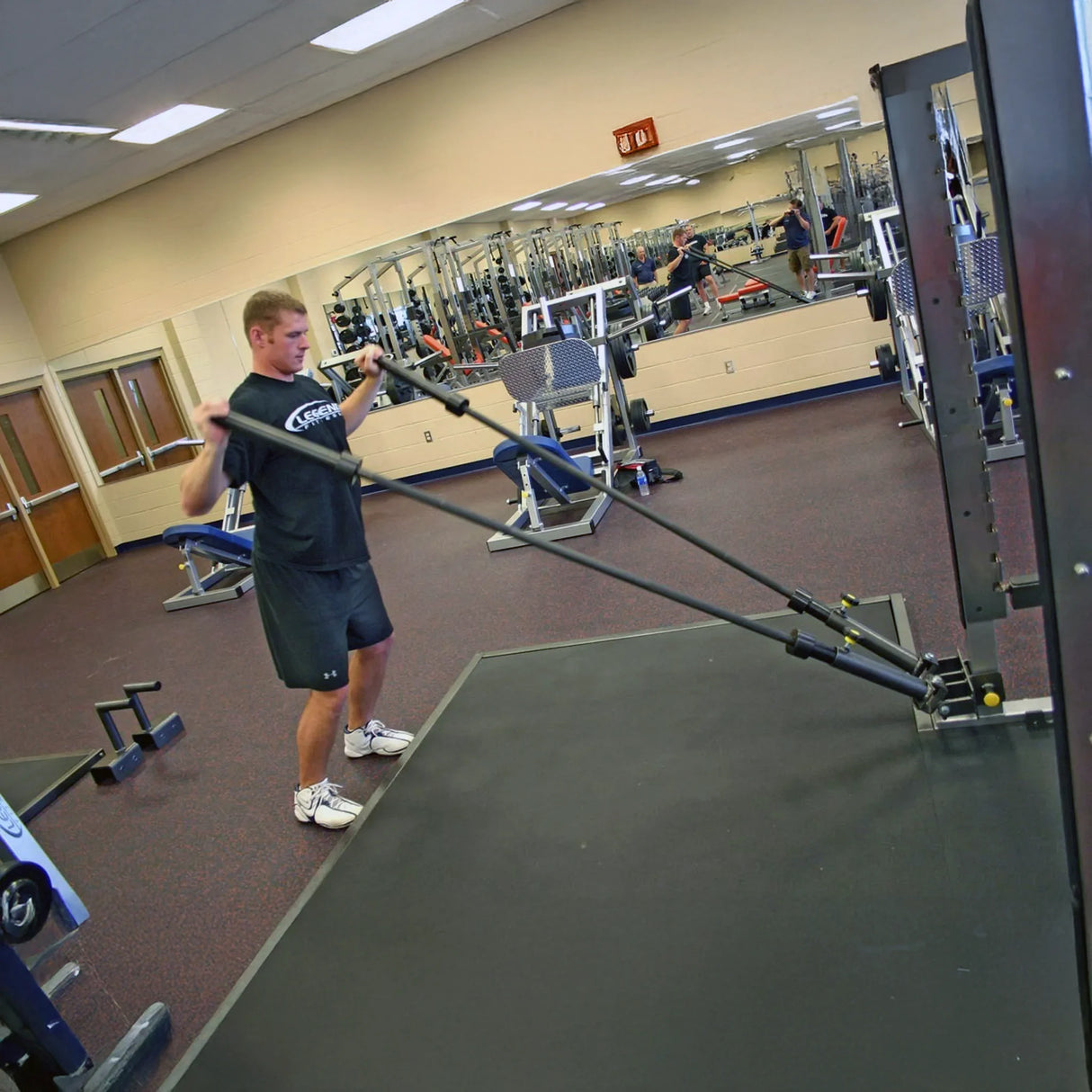A man exercising while holding one barbell in each hand which are stowed in a metal dual landmine attachment mounted to a squat