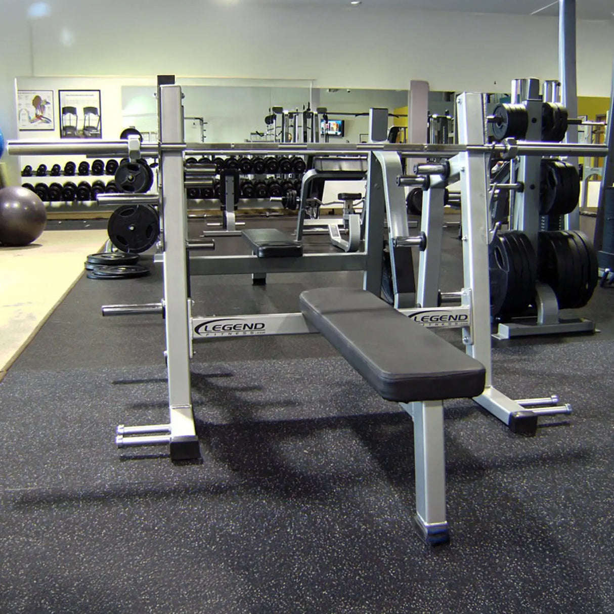 A silver and black Olympic flat bench press in a gym setting