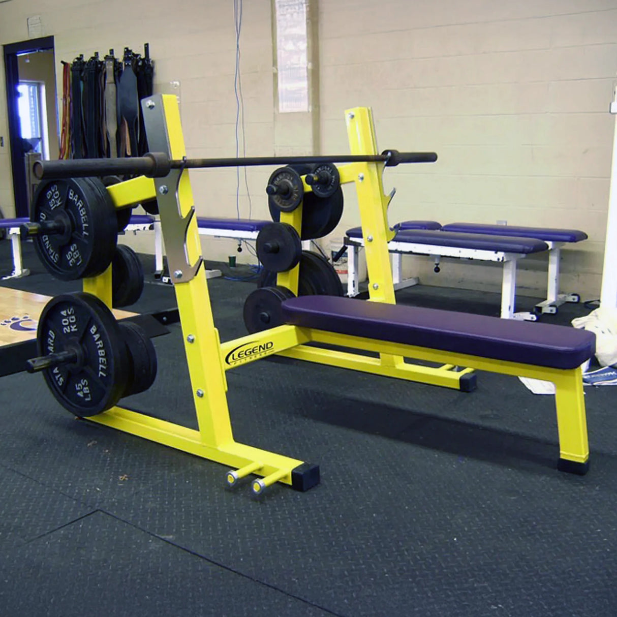 A yellow and purple Olympic flat bench press in a gym setting