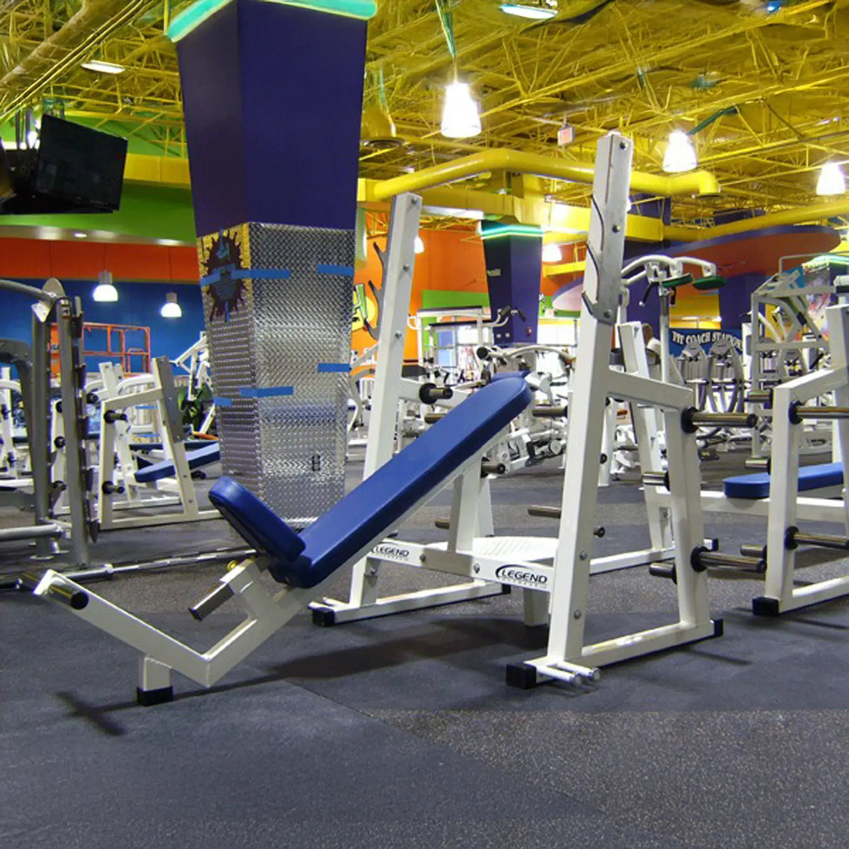 A white Olympic incline bench press with a blue pad in a gym setting