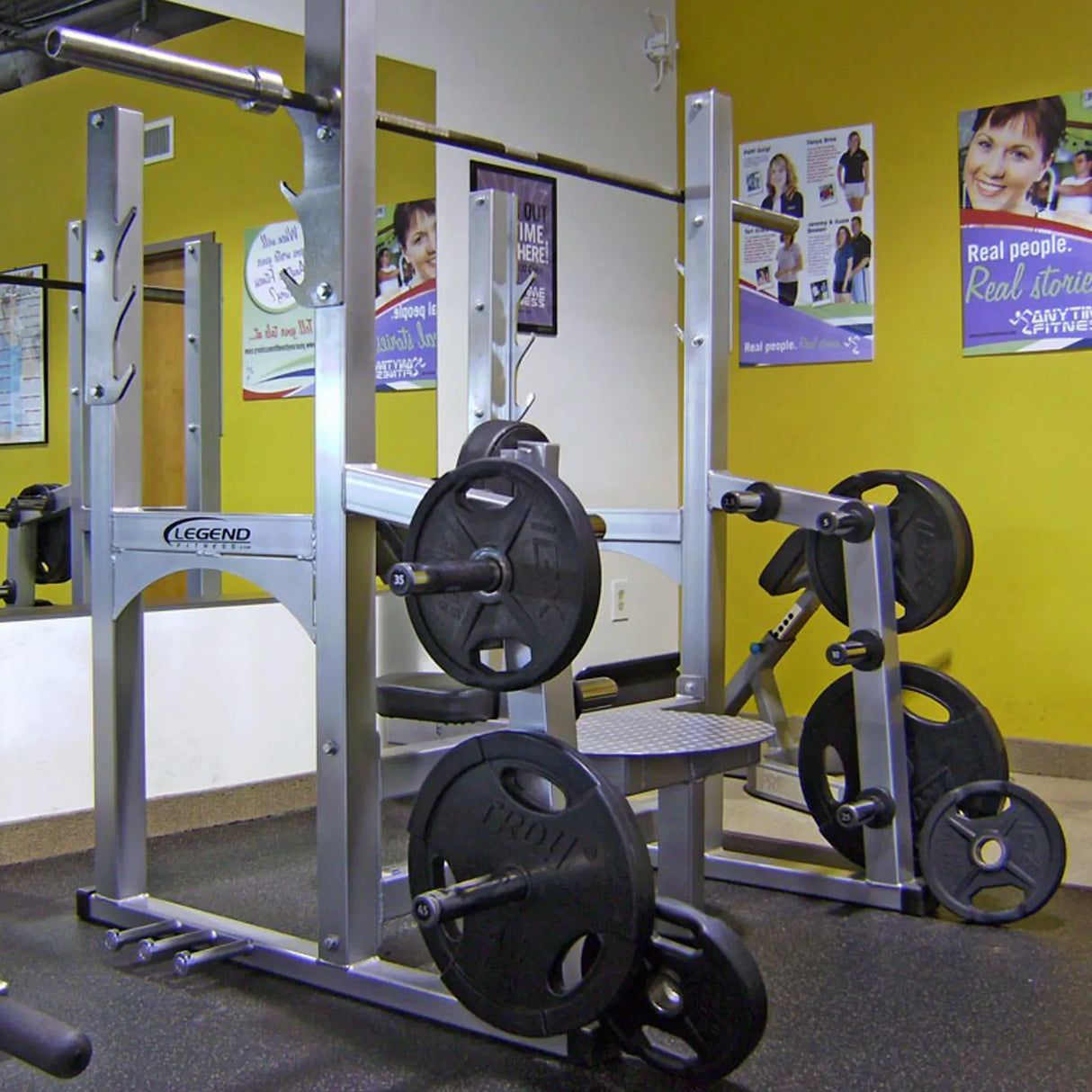 A silver Olympic shoulder press bench with black plates in a gym.