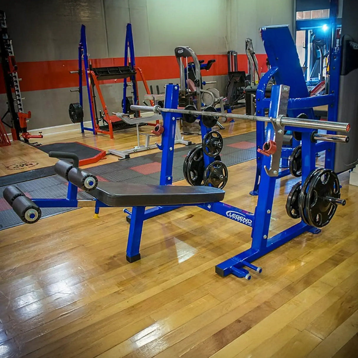A blue and black Olympic decline bench press on a wooden floor in a gym setting