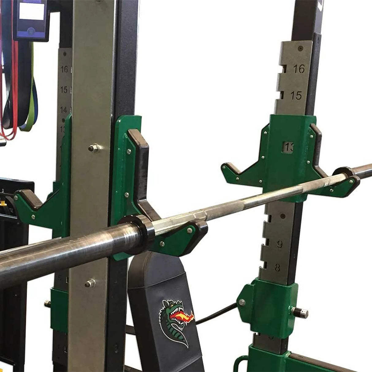 Green and black double-sided barbell hooks with a barbell stowed on one side mounted on a vertical metal upright with a bench on a white background