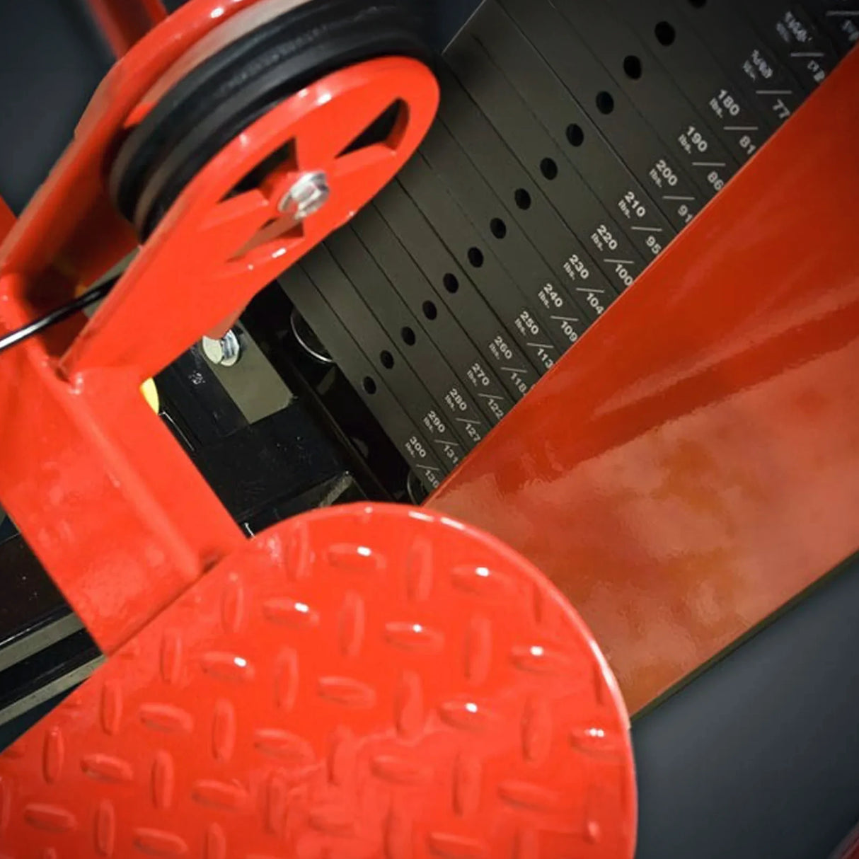 Close-up of a red metal weightlifting component with a black pulley on a black surface