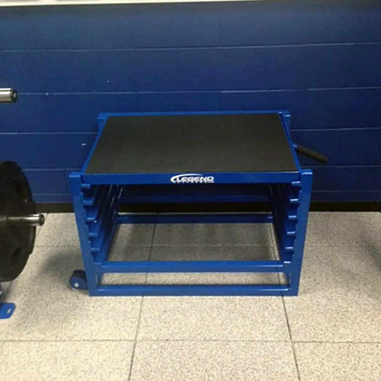 A blue metal adjustable step up box against a blue wall on a white floor in a gym setting