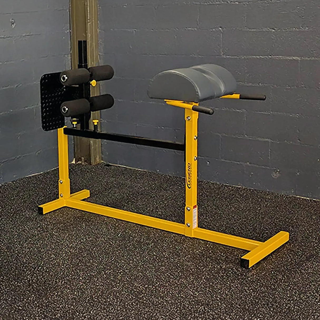 A yellow glute ham developer with black pads in a gym setting