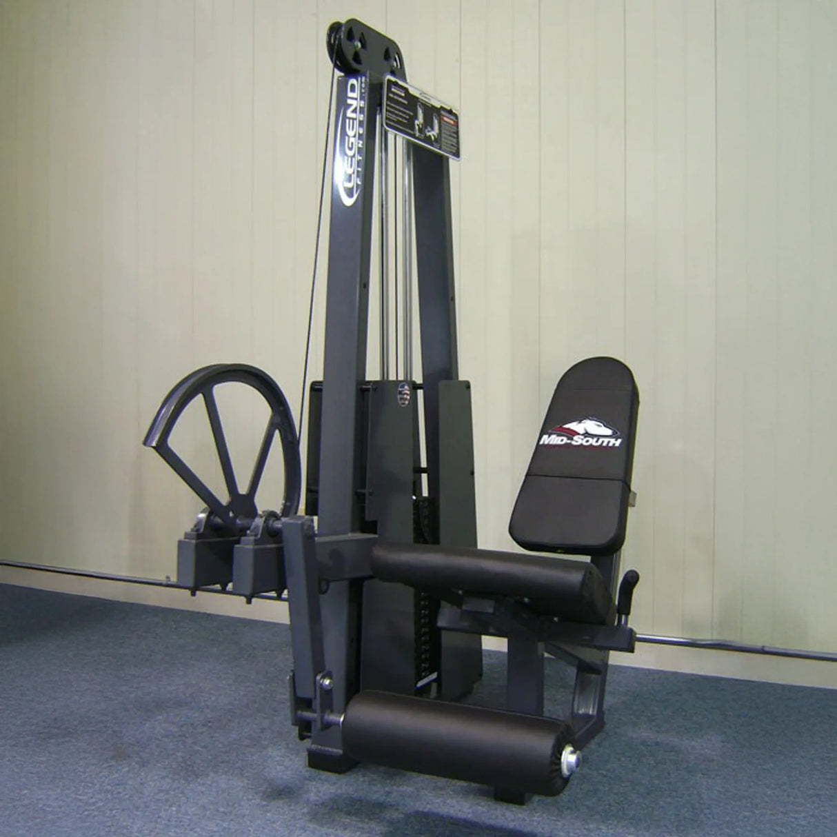 The Legend Fitness 911 Leg Extension Machine by Legend Fitness, featuring a padded seat and rollers in black, is set on blue carpet against a plain light-colored wall.