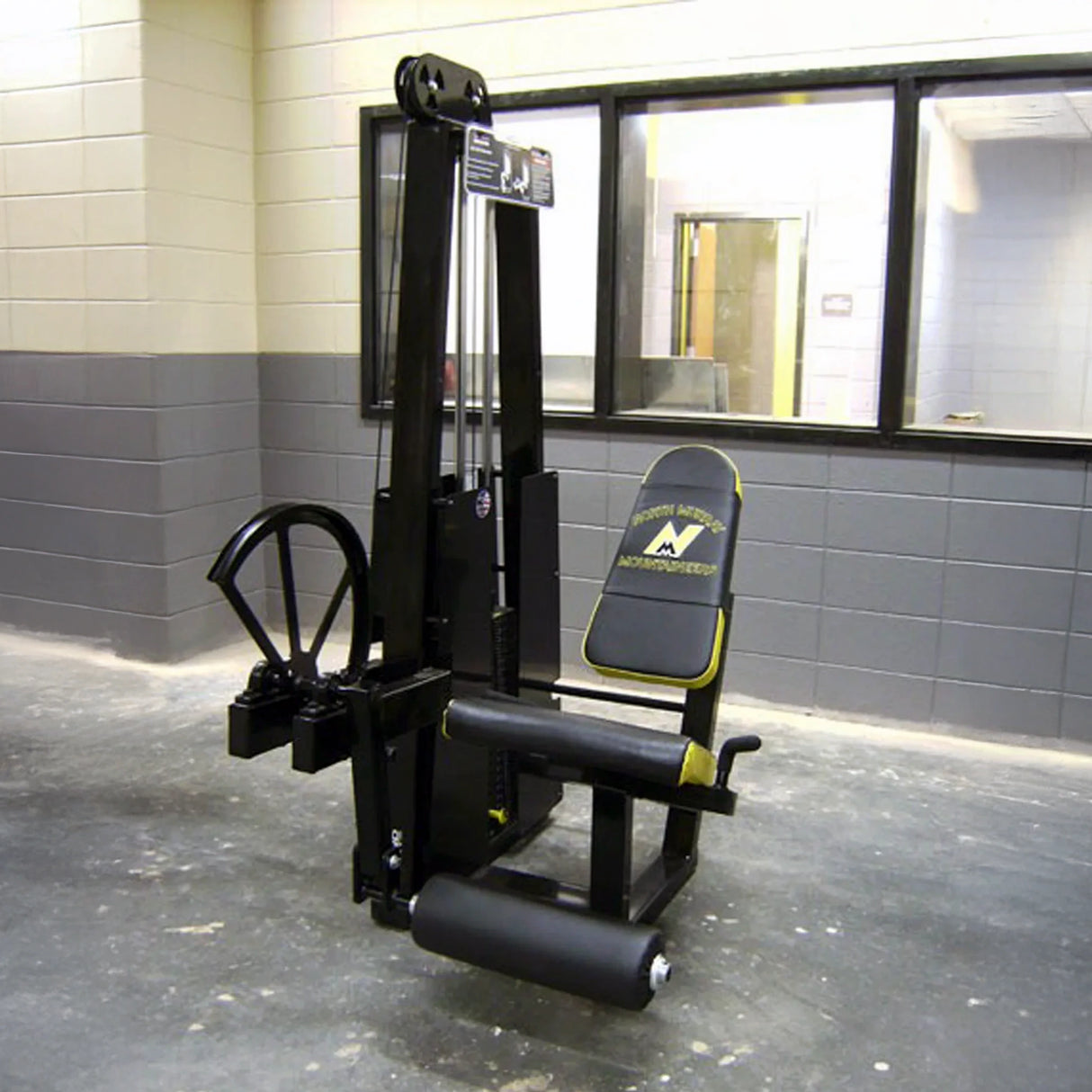 A Legend Fitness 911 Leg Extension Machine, featuring a black and yellow design, is set in a gym with gray and beige walls and large windows in the background.