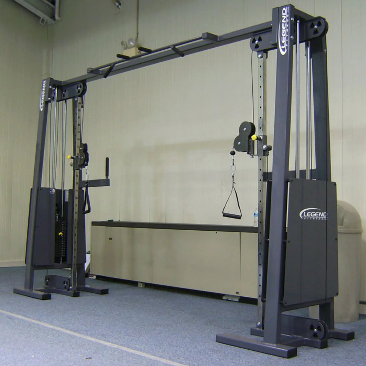 The Legend Fitness 954 Cable Crossover with Adjustable Pulleys and handles stands on a carpeted gym floor with beige walls, featuring the Legend Fitness brand.