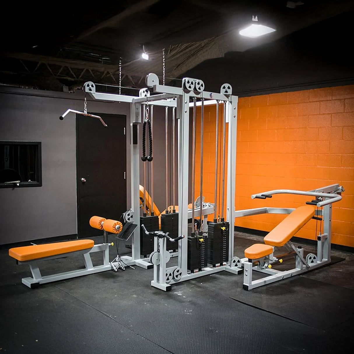 The Legend Fitness 958 Four-Stack Jungle Gym by Legend Fitness features orange and gray benches, cable pulleys, weights, and attachments in a modern gym with black and orange walls and a black rubberized floor.