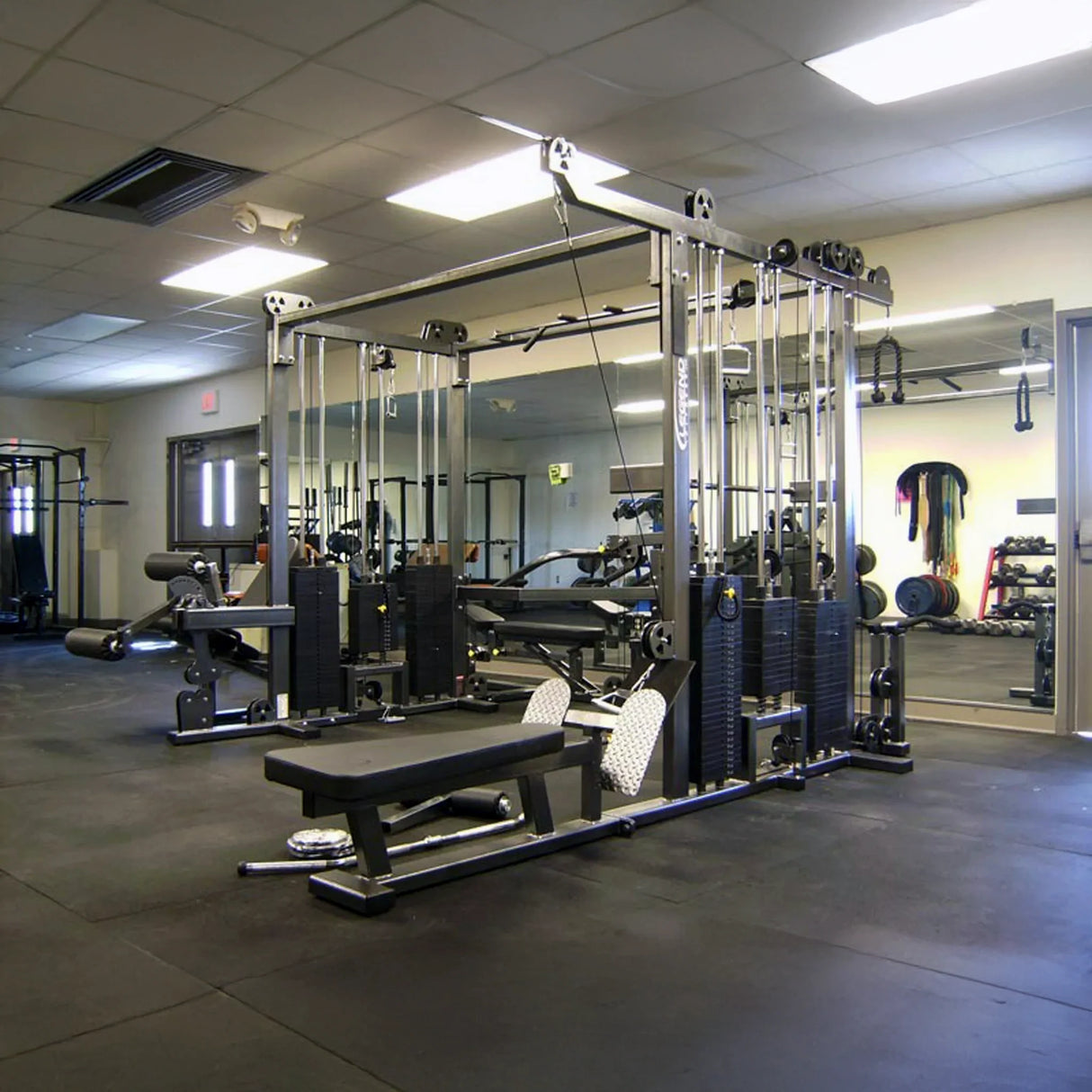 A clean, modern gym featuring the Legend Fitness 965 Combo Jungle Machine by Legend Fitness, benches, wall mirrors, and neatly organized gym equipment in a spacious, well-lit room with a black rubber floor.