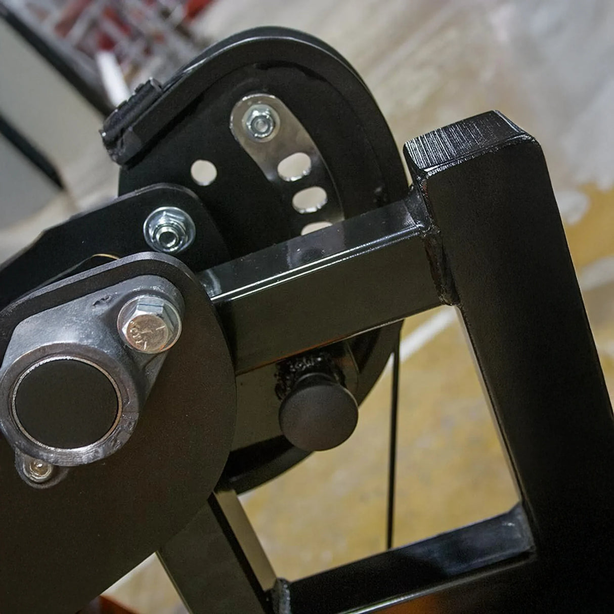 Close-up of the Legend Fitness 974 Pro Reverse Back Extension Machine, a black metal component with bolts and a circular joint by Legend Fitness, set against a blurred workshop background.