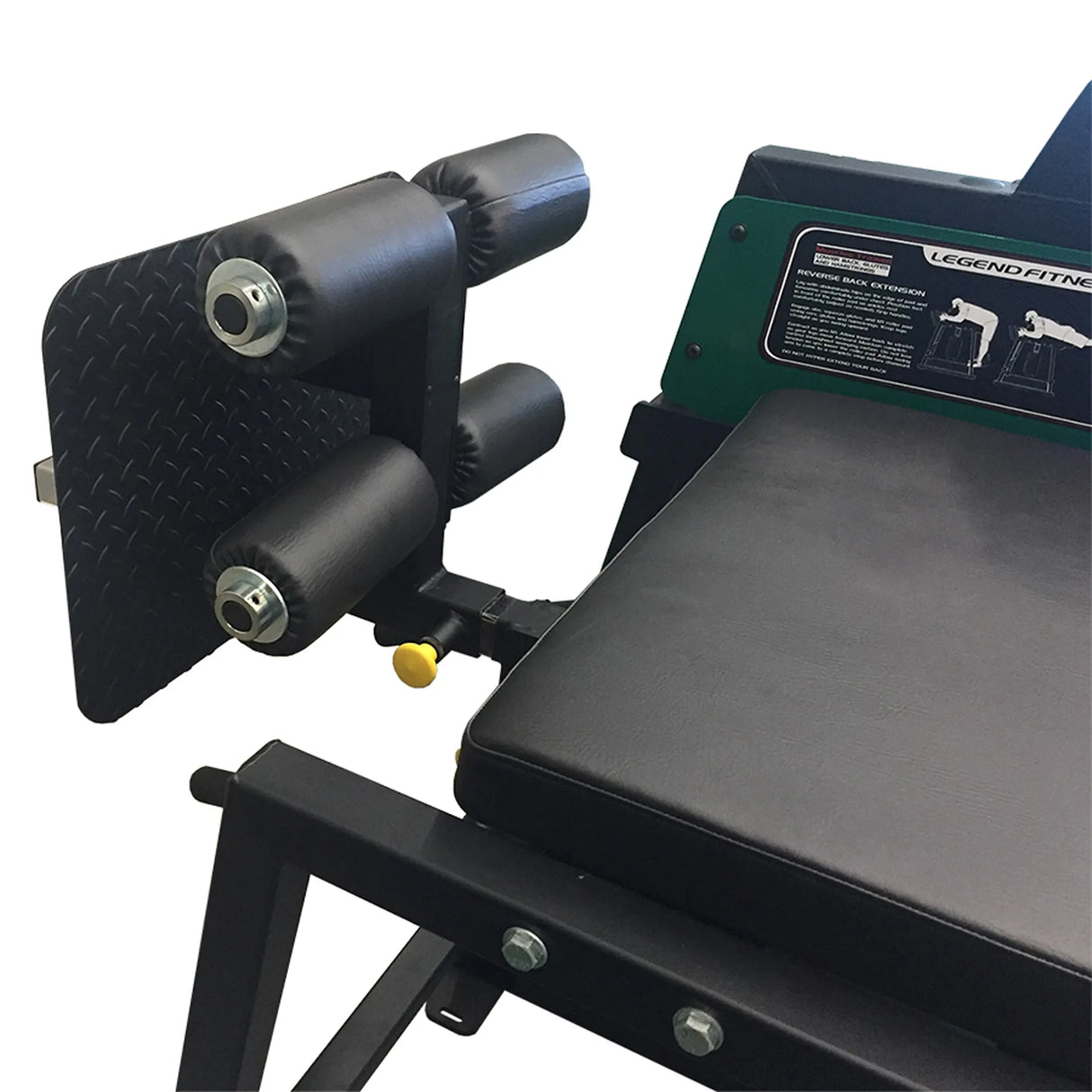 Close-up of the Legend Fitness 976-GH Reverse Back Extension/GHD Combo Machine, featuring black padded rollers, a diamond-plate footrest, part of a cushioned seat, visible adjustment knobs, and instruction labels on the Legend Fitness frame.