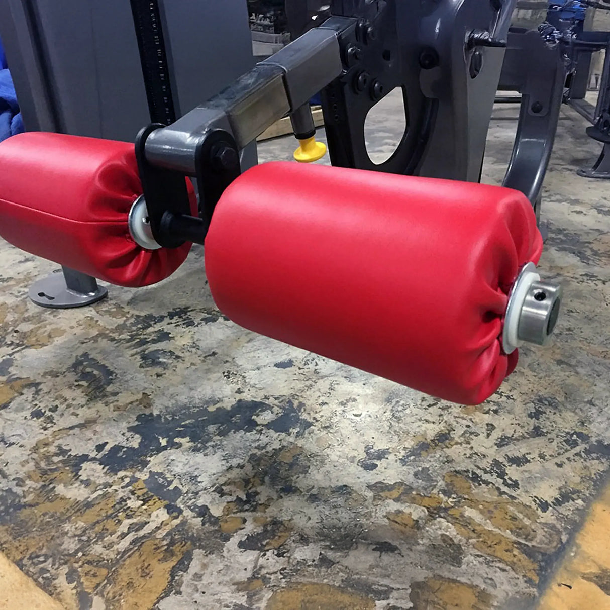 Red leg roller pads on a gym machine on a concrete floor