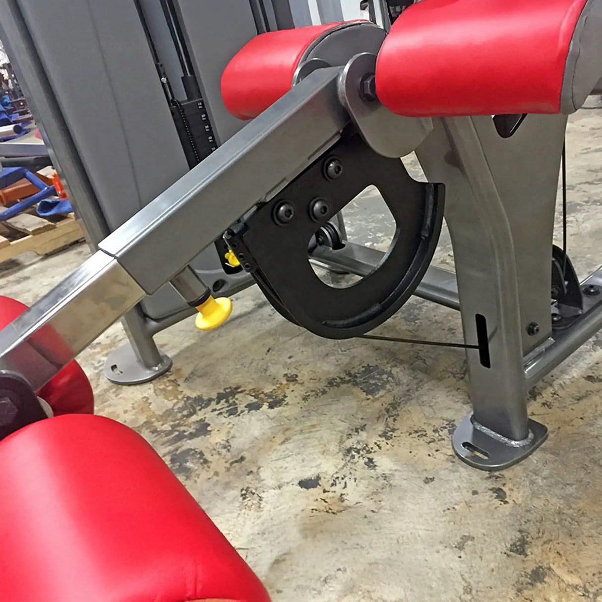 Close-up of a gym machine with red padding and gray metal components on a concrete floor.