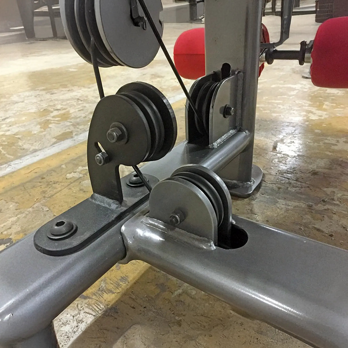 Close-up of a gray gym machine with pulleys and cables on a tiled floor.