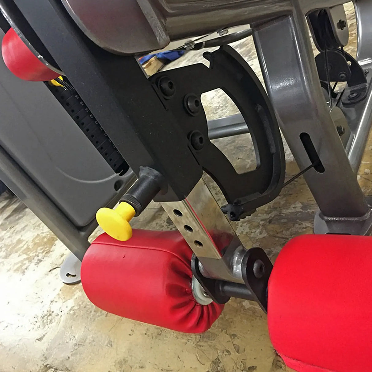 Close-up of a gym machine with red padding and black metal frame.