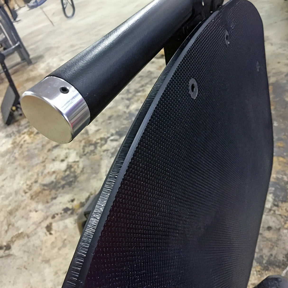 Close-up of a black footplate with a metallic handle on a blurred concrete floor