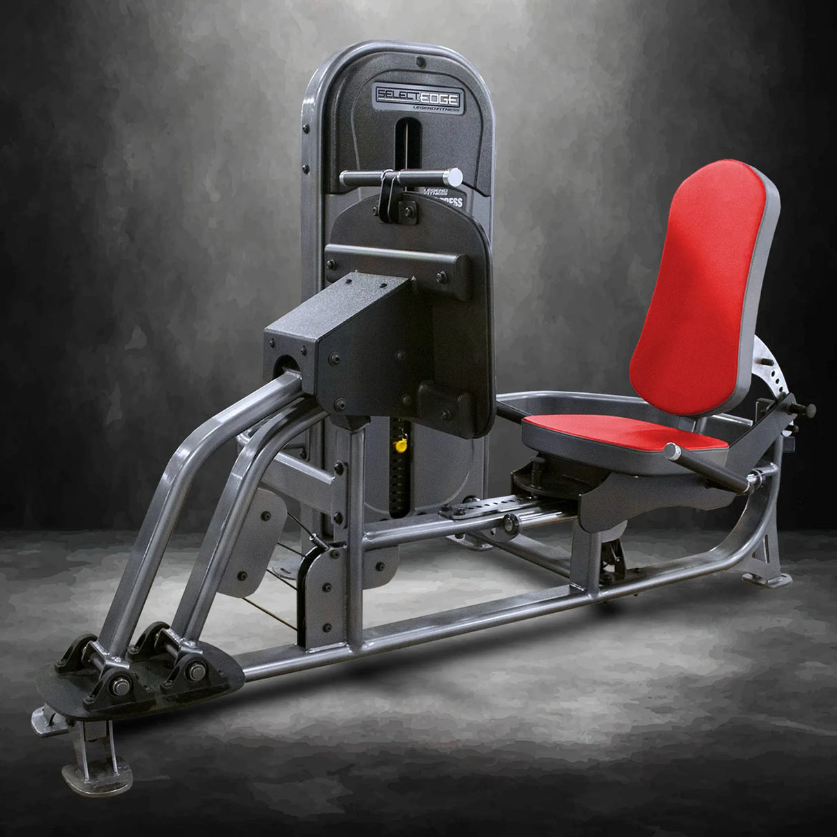 Gym leg press machine with red seat and gray frame on a dark background
