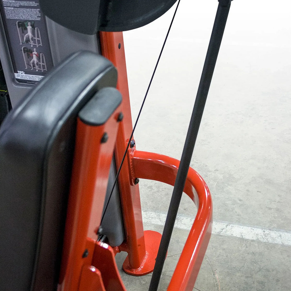 Close-up of a red exercise machine with black seat and handle on a concrete floor.