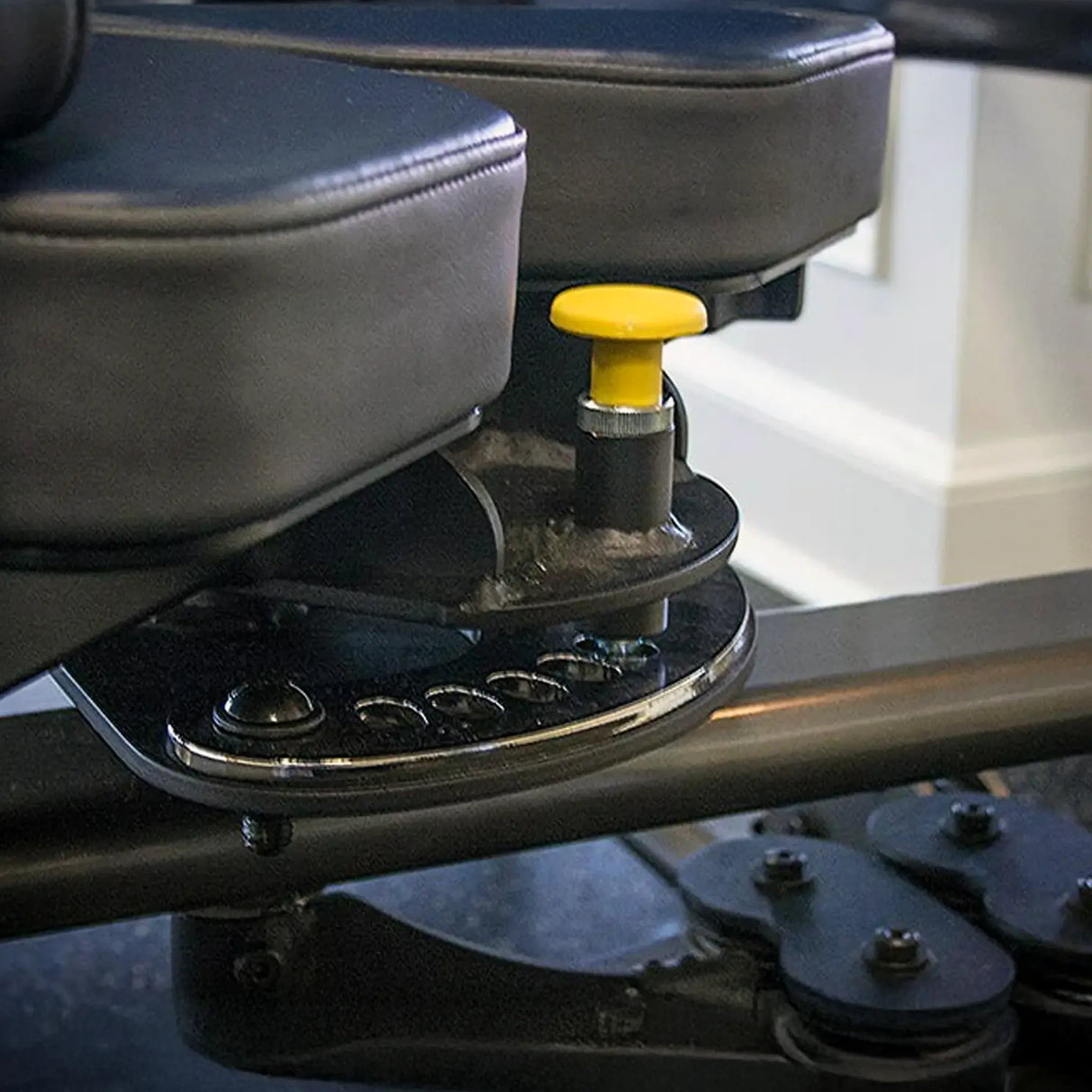 Close-up of a blue and gray workout machine seat with a yellow knob.