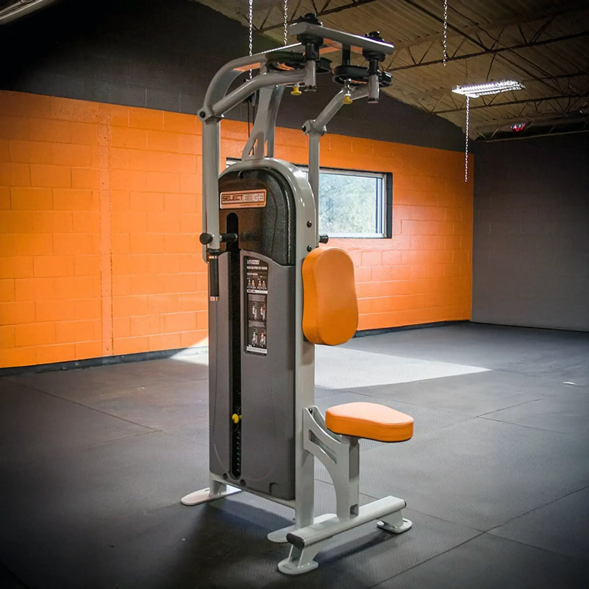 Gym machine with orange padding against an orange brick wall
